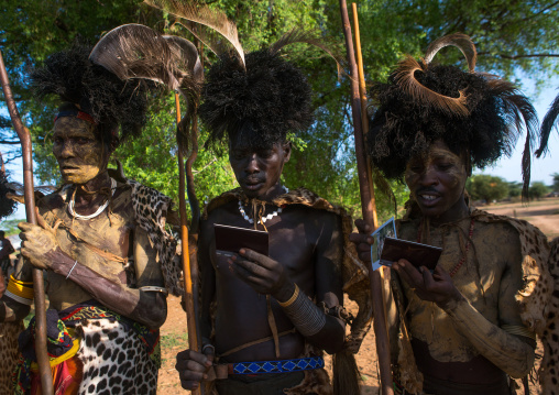 Dassanech tribe men looking polaroid pictures of themselves, Omo valley, Omorate, Ethiopia
