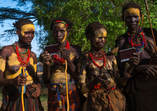 Dassanech tribe women looking polaroid pictures of themselves, Omo valley, Omorate, Ethiopia