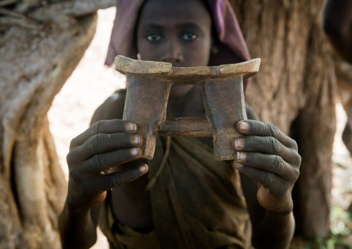 Circumcised boy from the dassanech tribe with his traditional wooden seat, Omo valley, Omorate, Ethiopia