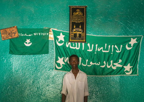 Sufi young man worshipper in front of islamic flags, Harari region, Harar, Ethiopia