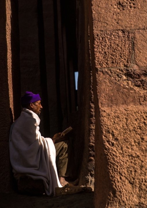 Lonely ethiopian orthodox man praying with a bible, Amhara region, Lalibela, Ethiopia