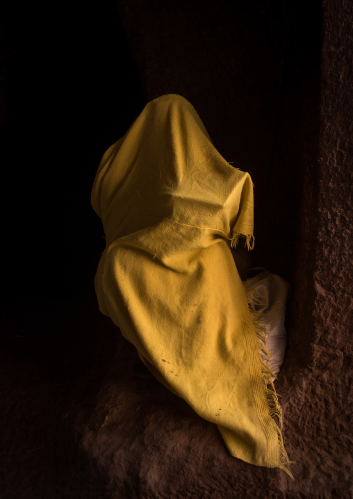 Orthodox woman covered with a yellow shawl praying with a bible, Amhara region, Lalibela, Ethiopia