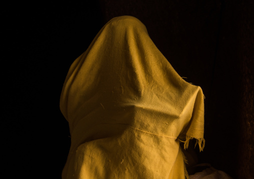 Orthodox woman covered with a yellow shawl praying with a bible, Amhara region, Lalibela, Ethiopia