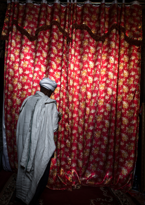 Orthodox priest praying with a bible in front of a curtain, Amhara region, Lalibela, Ethiopia