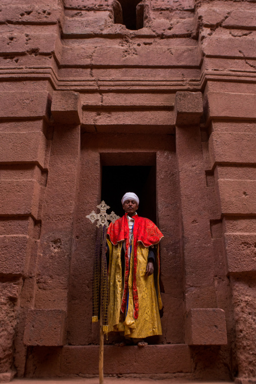Ethiopian orthodox priest holding a cross in front of a rock chrurch, Amhara region, Lalibela, Ethiopia