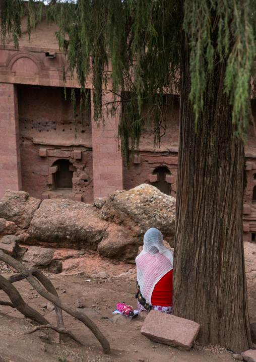 Lonely woman sit below a tree in front of a rock church, Amhara region, Lalibela, Ethiopia