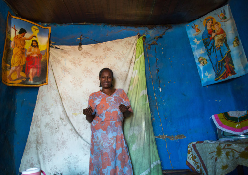 Woman inside her house decorated with religious posters, Omo valley, Jinka, Ethiopia