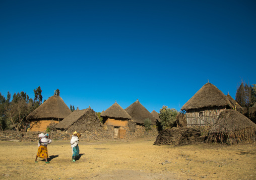 Two ethiopian women passing in front of stone houses village in the highlands, Amhara region, Debre Birhan, Ethiopia