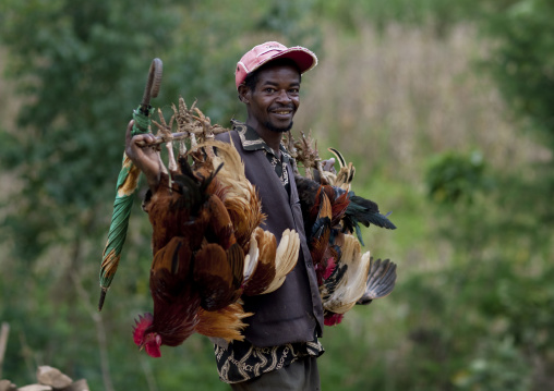 Benje man carrying chickens tied on a stick, Ethiopia