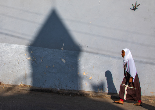 Ethiopian woman passing in front of the shadow of a mosque minaret in the street, Harari region, Harar, Ethiopia