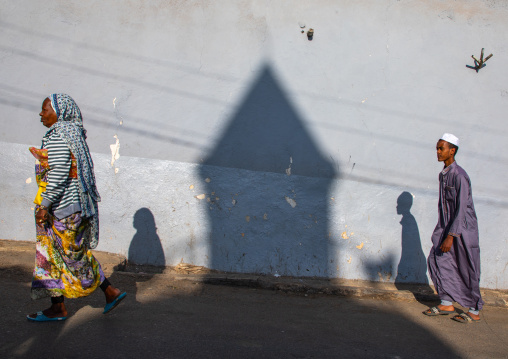 Ethiopian people passing in front of the shadow of a mosque minaret in the street, Harari region, Harar, Ethiopia
