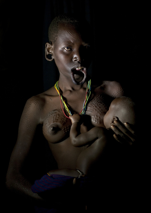 Suri Woman With Stretched Lip Breast Feeding Her Baby, Turgit Village, Omo Valley, Ethiopia