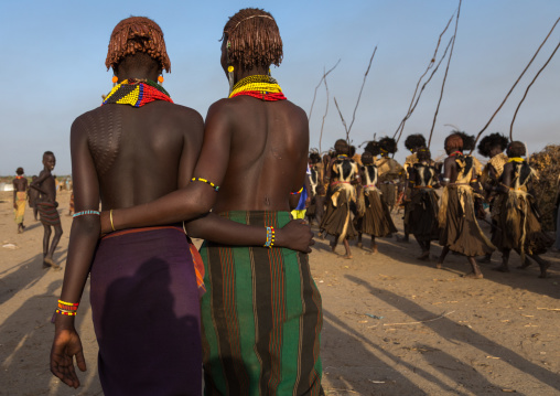 Girls looking at Dassanech men with leopard skins and ostrich feathers wigs during Dimi ceremony to celebrate circumcision of teenagers, Turkana County, Omorate, Ethiopia