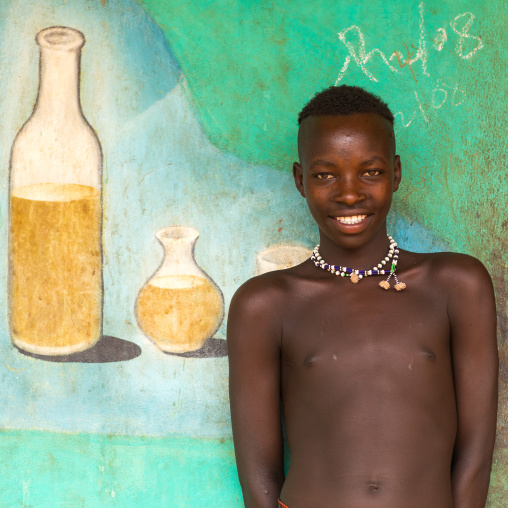 Young Bana tribe boy in front of a painted mural for tej drink in a bar, Omo valley, Key Afer, Ethiopia