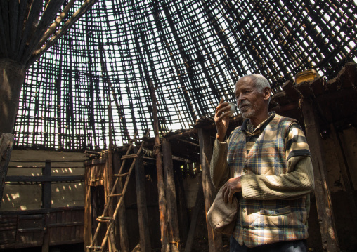 Old man drinking a coffee under a Gurage traditional roof without thatch in renovation, Gurage Zone, Butajira, Ethiopia