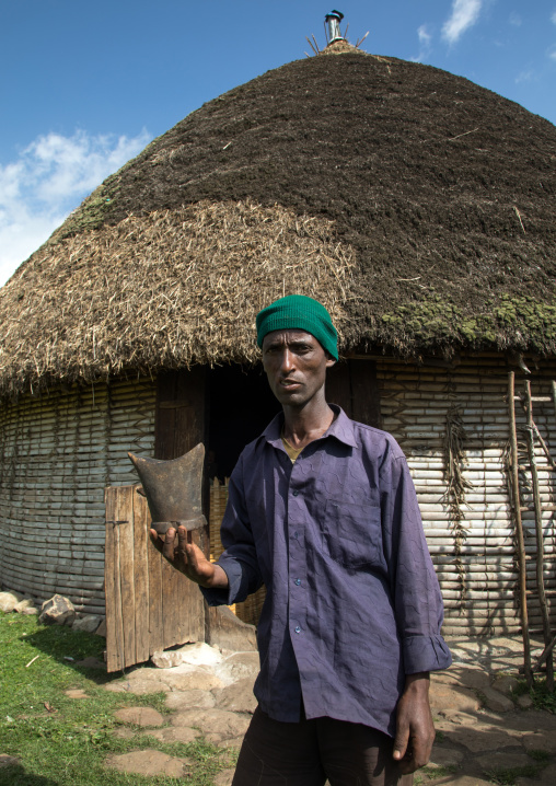 Gurage tribe man with his traditional wooden pillow in front of his house with tatched roof, Gurage Zone, Butajira, Ethiopia
