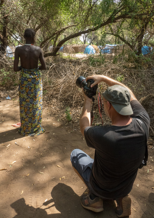 A tourist photographer taking a picture of a sudanese toposa tribe woman with scarifications, Omo valley, Kangate, Ethiopia
