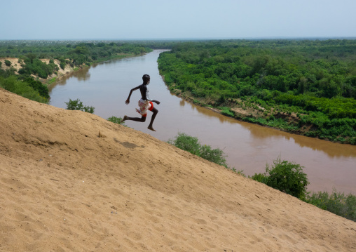 Karo tribe boy jumping in front of Omo river bank, Omo valley, Korcho, Ethiopia