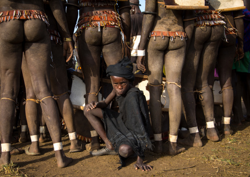 Child boy in the middle of Bodi tribe fat men legs during Kael ceremony, Omo valley, Hana Mursi, Ethiopia