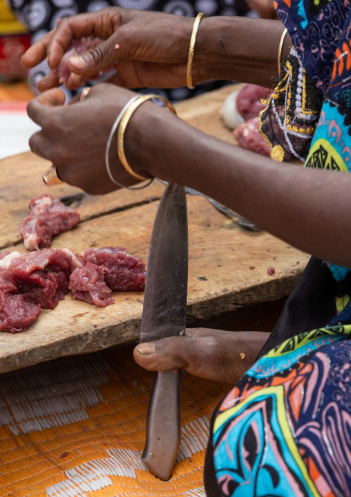 Harari woman cutting meat with a knife she holds with her foot, Harari Region, Harar, Ethiopia