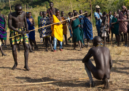 Suri tribe warrior putting a knee on the ground to show he lost the donga stick fighting, Omo valley, Kibish, Ethiopia