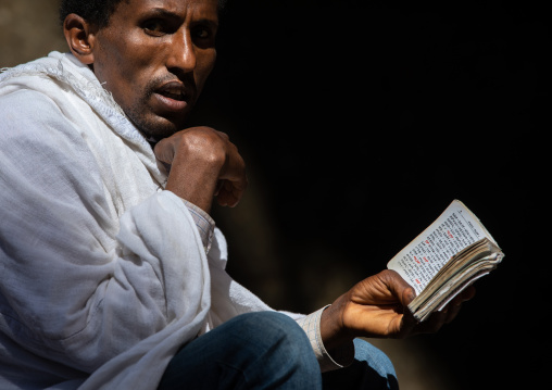Orthodox man praying with a bible, Amhara Region, Lalibela, Ethiopia