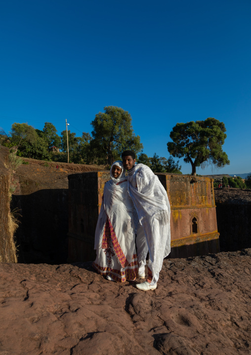 Ethiopian new wed couple pausing in front of the monolithic rock-cut church of bete giyorgis, Amhara Region, Lalibela, Ethiopia