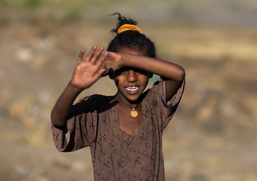 Ethiopian girl waving hand and protecting from the sun, Amhara Region, Lalibela, Ethiopia