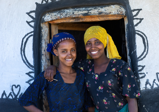 Smiling raya tribe gilrs at the entrance of a decorated hut, Afar Region, Chifra, Ethiopia
