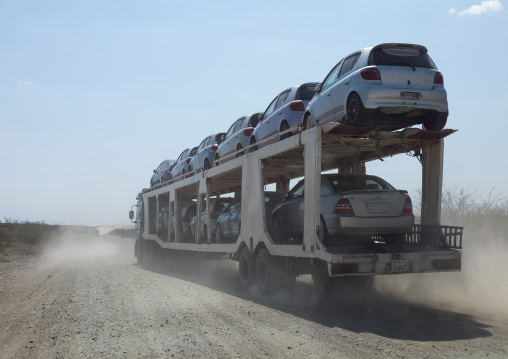 Truck carrying new cars coming from djibouti port on a dusty road, Oromia, Awash, Ethiopia