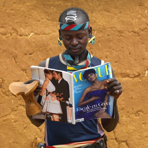 Young fashionable banna tribe man with headrest watching vogue  magazine, Omo valley, Ethiopia