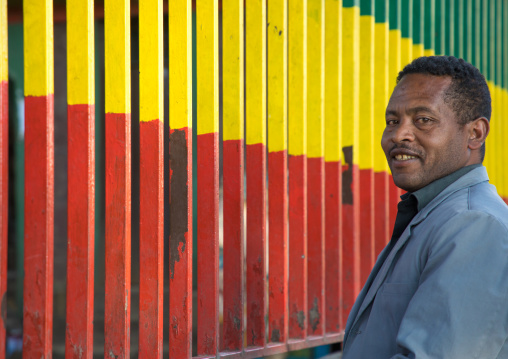 Ethiopian man standing in front a metal fence with the colors of the ethiopian flag, Addis Ababa Region, Addis Ababa, Ethiopia