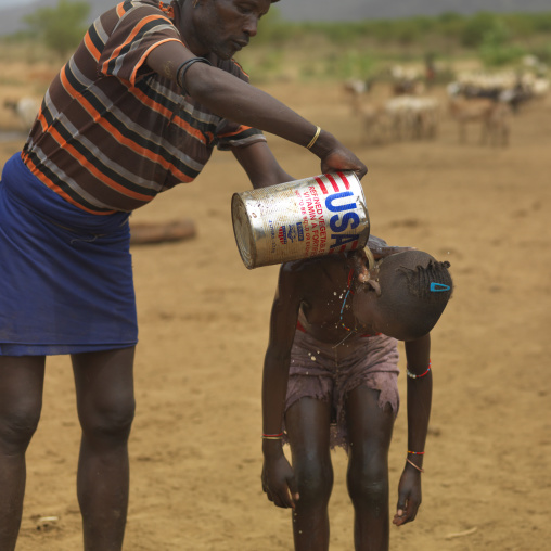 Tsemay tribe man washing his daughter with usa labeled can, Omo valley, Ethiopia