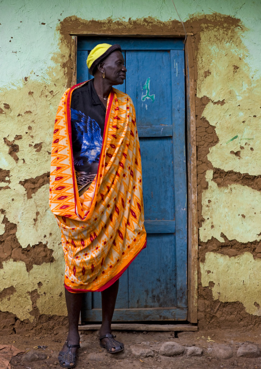 Portrait Of A Bodi Tribe Man In Orange Wrap Around Clothes Posing Outside A House, Hana Mursi, Omo Valley, Ethiopia