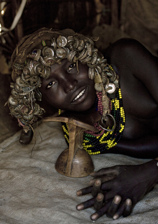 Portrait Of A Dassanech Tribe Girl With Wig Made Of Caps Using Headrest To Lay Down, Omorate, Omo Valley, Ethiopia
