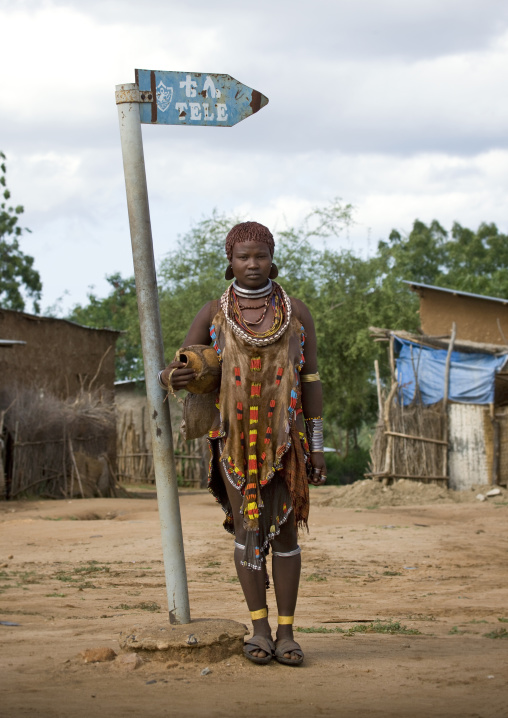 Hamar Tribe Woman With Traditional Clothes Posing Next To A Sign Indicating Where To Watch Tv, Turmi, Omo Valley, Ethiopia