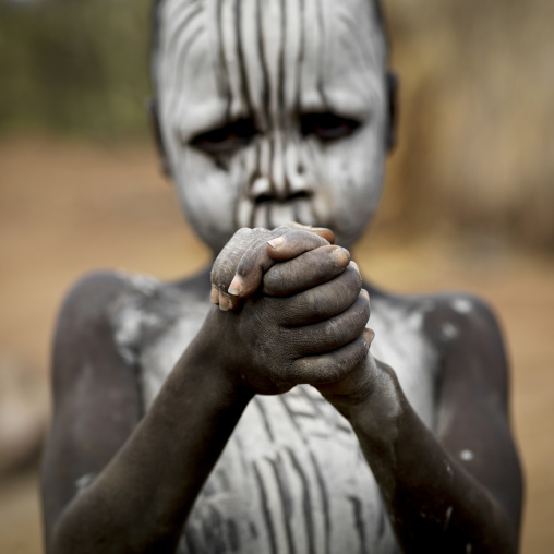 Mursi Boy With White Painted Face Holding His Two Hands, Omo Valley, Ethiopia