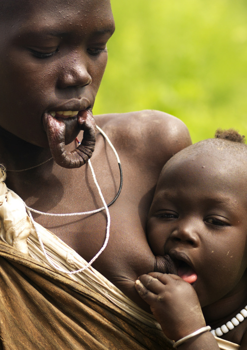 Portrait Of A Mursi Tribe Mother Brestfeeding Her Baby, Omo Valley, Ethiopia