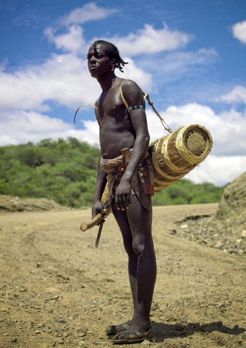 Young tsemay tribe carrying axe and wickerwork container on his back to collect honey, Omo valley, Ethiopia