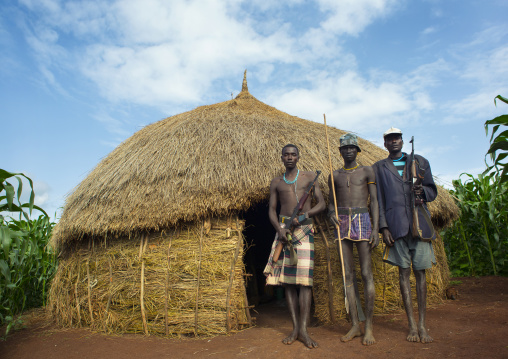 Menit tribe men displaced by governement holding guns in front of their new houses, Jemu, Ethiopia