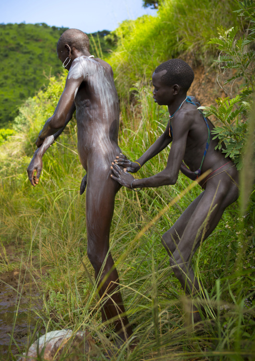 Shepherd from Suri tribe receiving help to decorate his body with camouflage paintings, Tulgit, Omo valley, Ethiopia