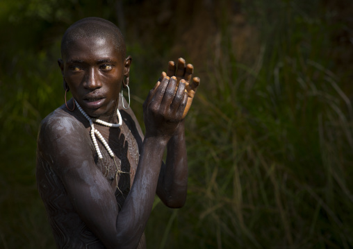 Shepherd from Suri tribe decorating his body with camouflage paintings, Tulgit, Omo valley, Ethiopia