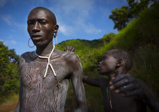 Shepherd from Suri tribe receiving help to decorate his body with camouflage paintings, Tulgit, Omo valley, Ethiopia