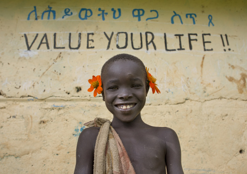 Young Suri boy leaning against a wall of a school, Covered with amharic and english writing, Tulgit, Omo valley, Ethiopia