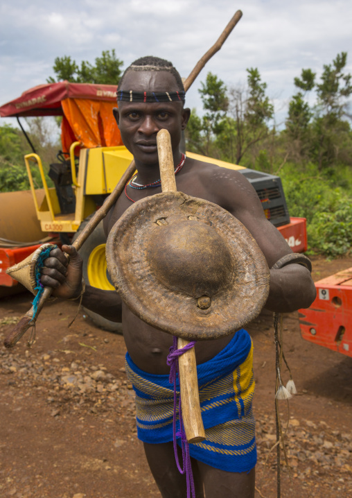 Bodi Tribe Warrior Posing Proudly With A Shield Near A Bulldozer Near Hana Mursi, Omo Valley, Ethiopia