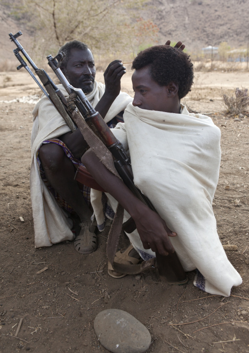 Karrayyu Tribe Man Squatting With His Kalashnikov While Having His Gunfura Traditional Hairstyle Done Before Gadaaa Ceremony, Metahara, Ethiopia