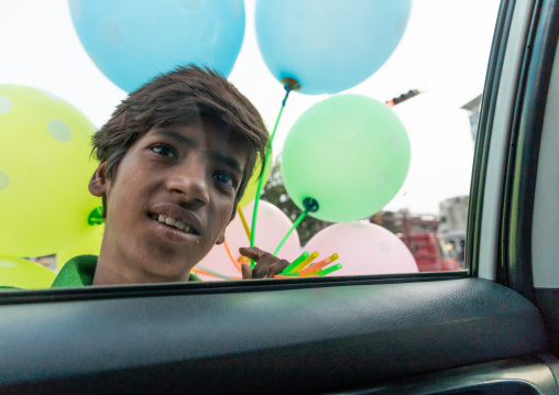 Indian hawker selling colorful balloons to a to tourist in a car, Rajasthan, Jaipur, India