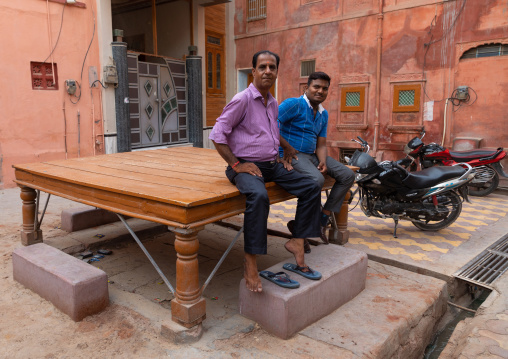 Indian men sit on a resting bed in front of a beautiful haveli in the old city, Rajasthan, Bikaner, India