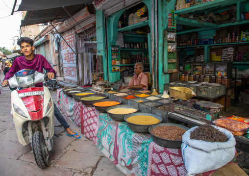 Indian man on a scooter passing by a shop selling spices, Rajasthan, Jodhpur, India