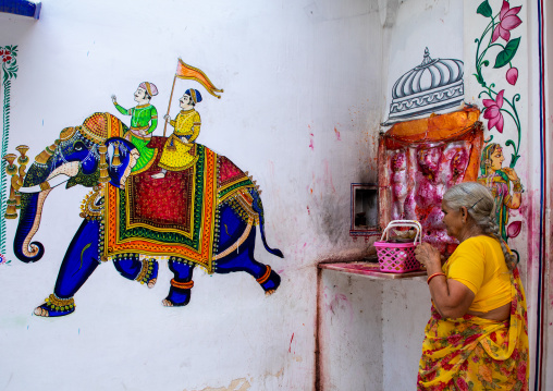 Indian woman praying in a temple decorated with murals depicting an elephant, Rajasthan, Udaipur, India